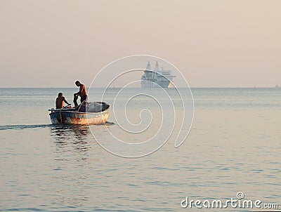 Albanian fishermen in their old fishing boat, big modern ship in the distance Editorial Stock Photo